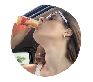 A woman wearing sunglasses with brown hair drinking a Vive Organic Shot.