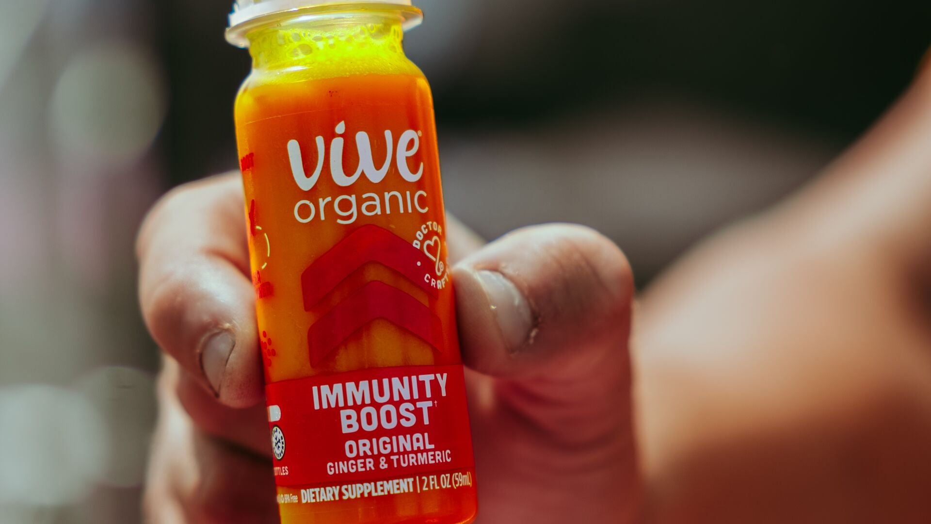 Hand holding a Vive Organic Immunity Boost Original ginger and turmeric wellness shot