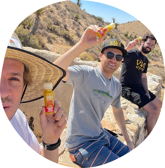 Wyatt, Kyle, and Jr. the Vive Organics founders holding up their vive shots on a hike in the desert mountains