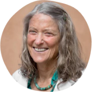 A smiling person with long gray hair wearing a necklace and white shirt.
