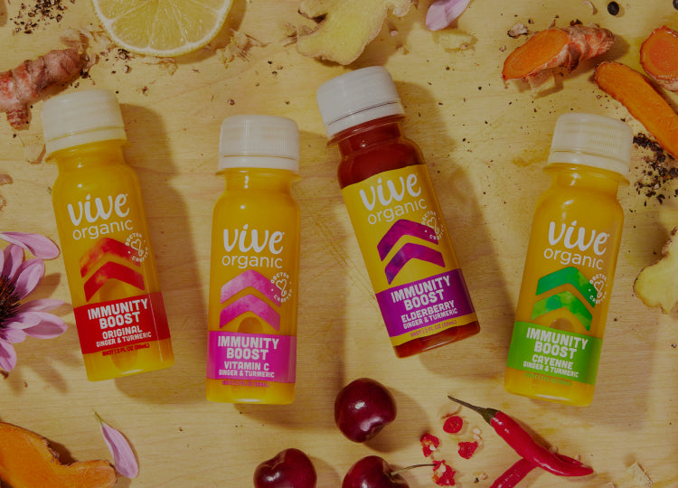 Image of Vive Organic Immunity Boost Shots collection laying flat on a cutting board surrounded by fresh echinacea flower, ginger, turmeric, acerola cherry, lemon and cayenne pepper.
