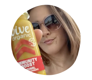 Woman wearing sunglasses with brown hair holding a Vive Organic Immunity shot original in her hand.